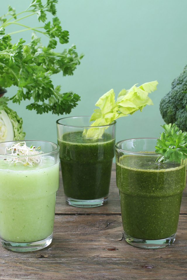 Зеленый овощной смузи в стаканах на столе со свежими овощами и яблоками