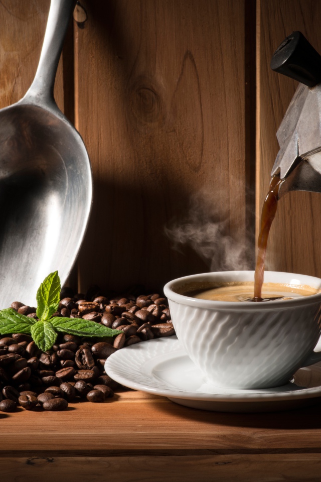 Горячий кофе наливают в белую чашку на столе с кофейными зернами