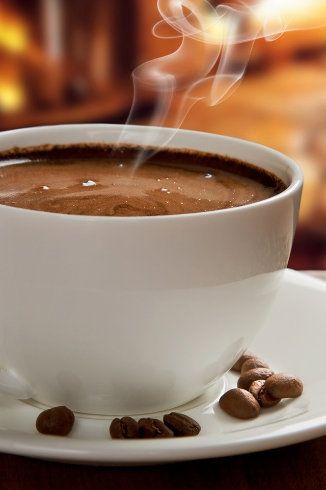 Большая белая чашка с горячим кофе на столе с кофейными зернами