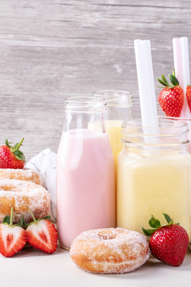Молочные коктейли на столе с пончиками и ягодами клубники 