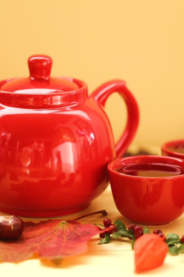 Красный чайник с чашками на столе осенью 