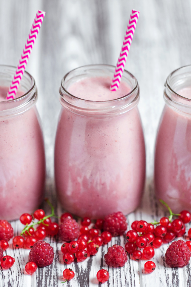 Три банки ягодного  смузи на столе с ягодами малины и смородины