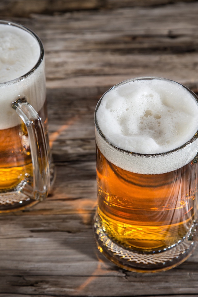 Два бокала пива с пеной на деревянном столе