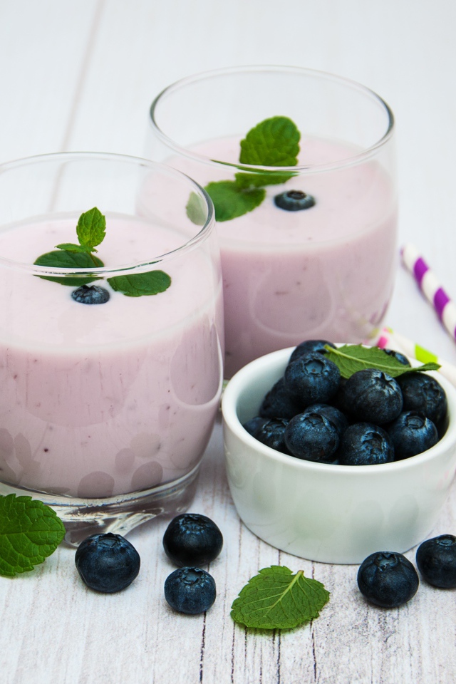 Два стакана коктейля в стаканах на столе с ягодами черники и трубочками