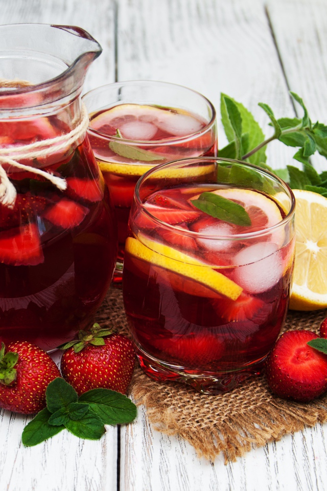 Два стакана мохито на столе с графином, лимоном, клубникой и мятой