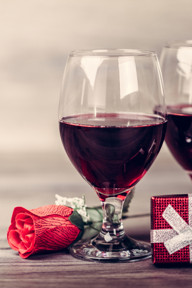 Два бокала вина на столе с подарками и красной розы 