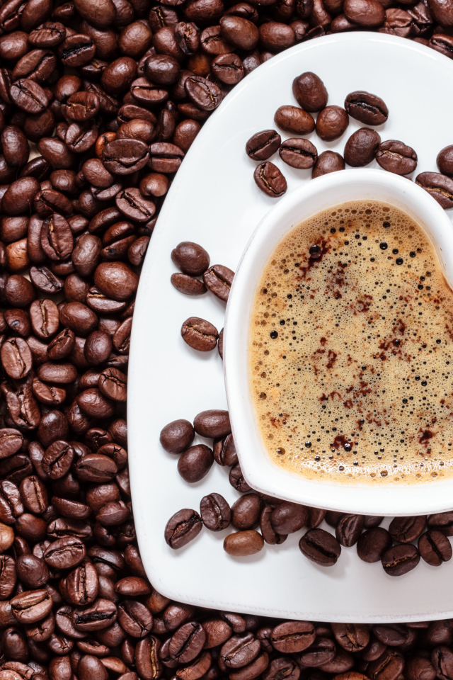 Белая чашка в форме сердца стоит на кофейных зернах 