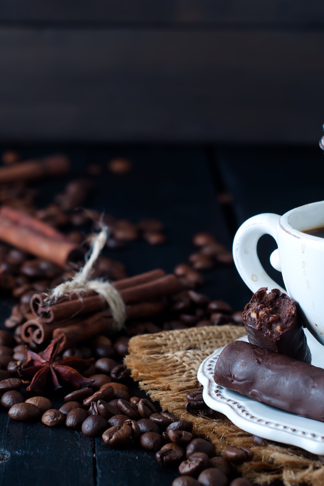Белая чашка кофе на столе с конфетами, корицей, бадьяном и зернами