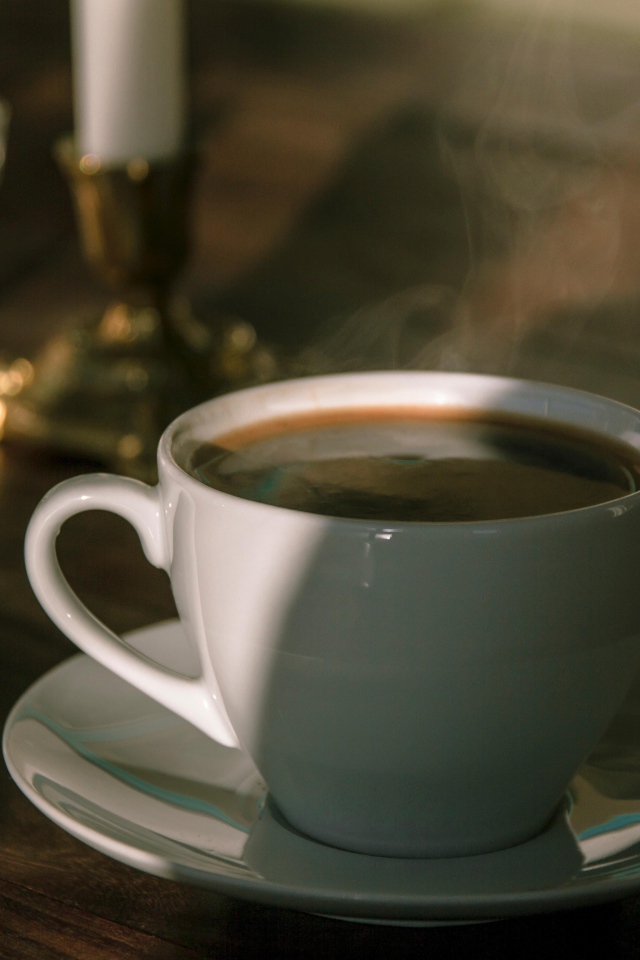 Белая чашка кофе на столе в лучах солнца