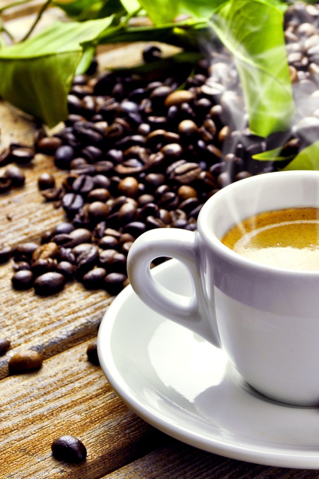 Белая чашка с горячим кофе на деревянном столе с кофейными зернами