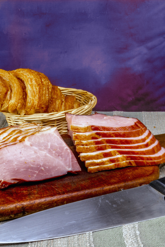 Кусок нарезанной ветчины на доске с круассаном