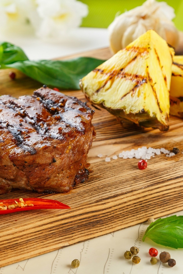 A piece of grilled meat on a wooden board with pineapple slices and basil