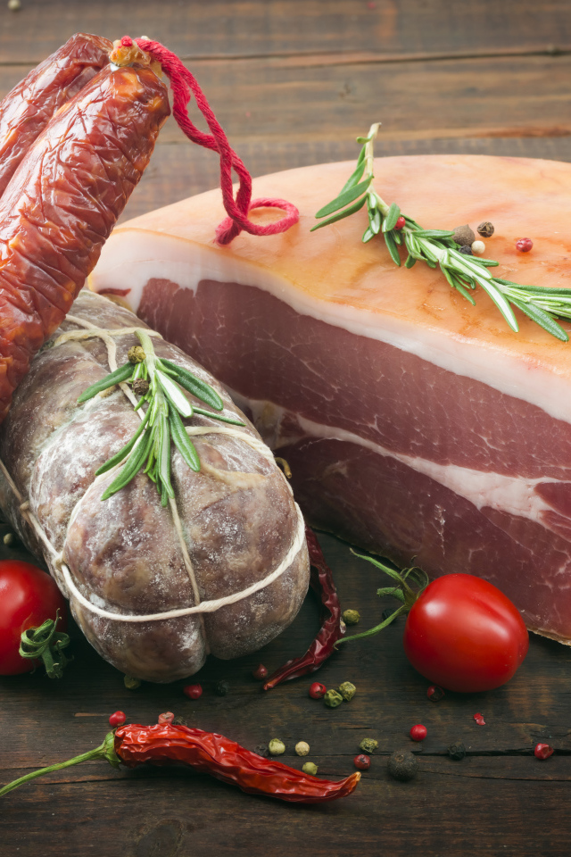 Кусок мяса и колбаса на деревянном столе с помидорами и специями