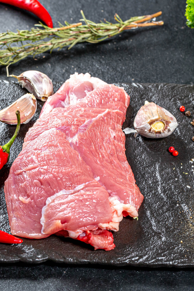 Кусок мяса на столе с острым перцем, чесноком и зеленью