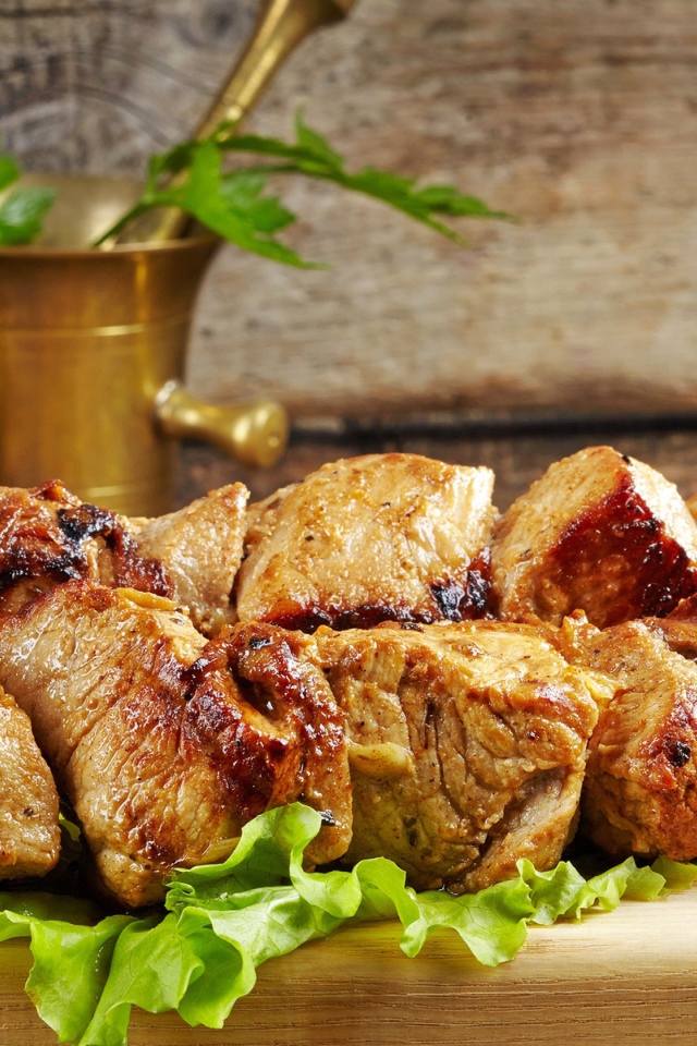 Аппетитный шашлык лежит на разделочной доске с листьями салата