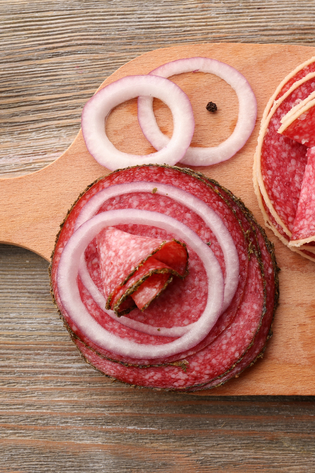 Аппетитные кусочки колбасы на разделочной доске с кольцами лука