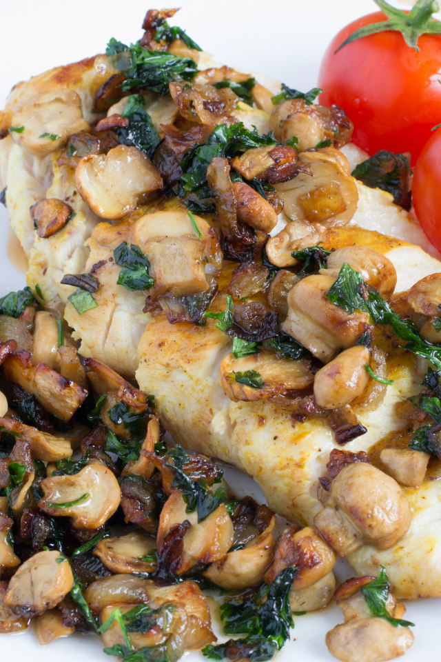 Аппетитный кусок куриного филе с грибами на тарелке с помидорами 