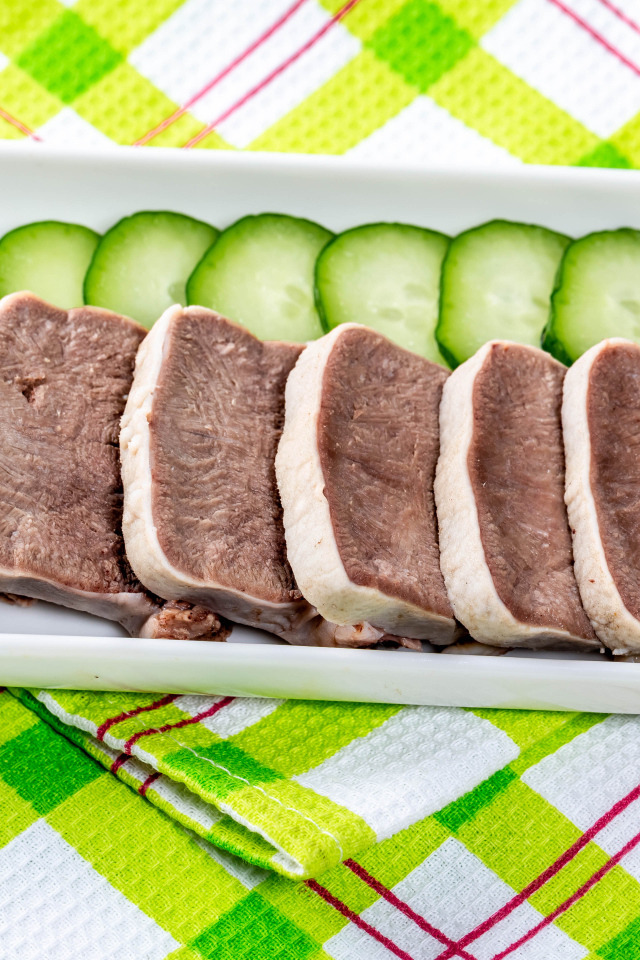 Вареный язык на тарелке со свежими огурцами