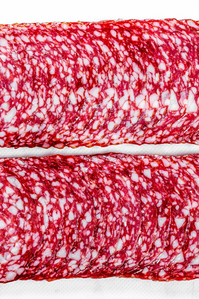 Колбаса салями нарезанная тонкими кусочками на белом фоне