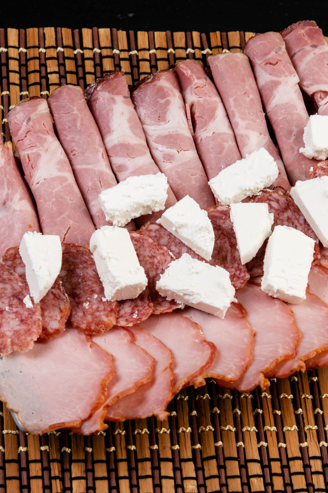 Колбаса и ветчина на тарелке с кусочками сыра фета