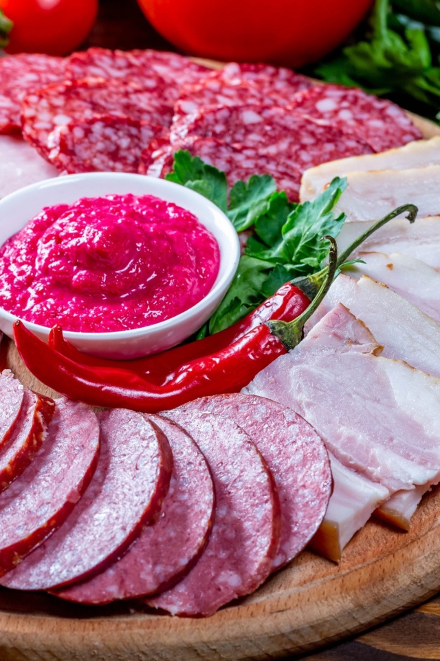 Мясная нарезка на доске с соусом, красным перцем,  помидорами и зеленью 