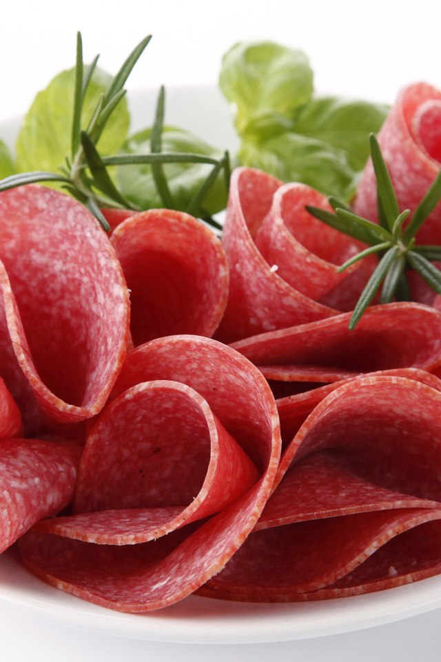 Тонкие кусочки колбасы на тарелке с зеленью 