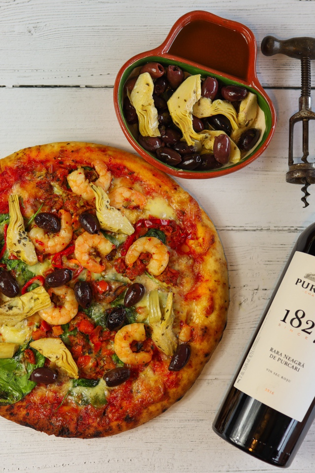 Пицца на столе с оливками и бутылкой вина