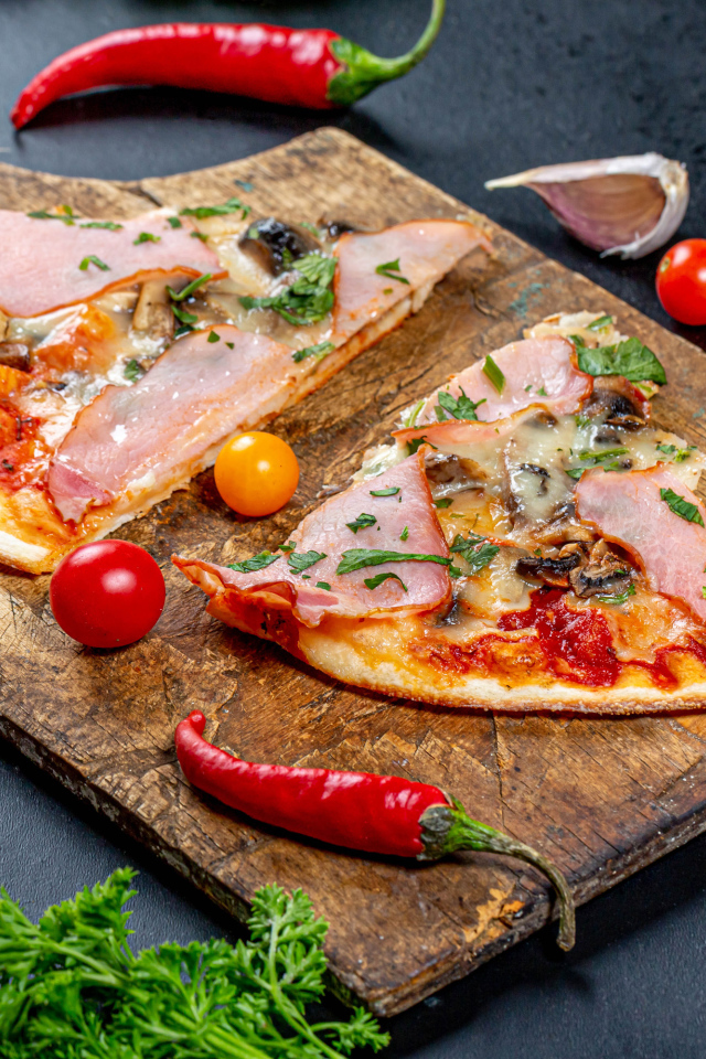 Два куска пиццы на разделочной доске с красным перцем и чесноком