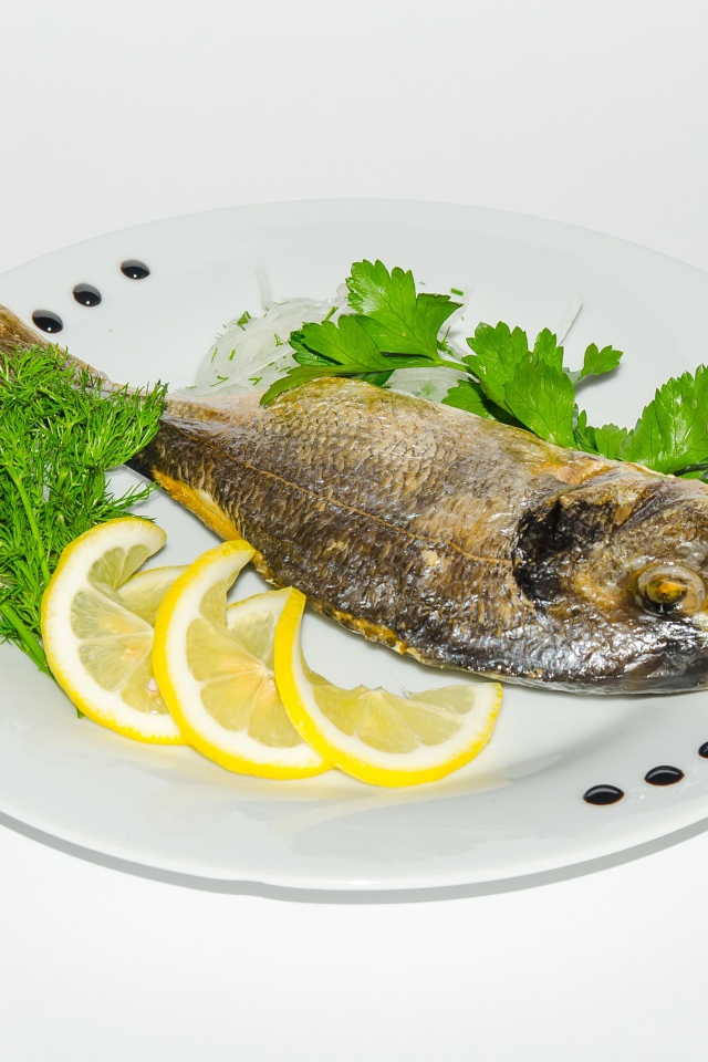 Запеченная рыба на тарелке с лимоном и зеленью 