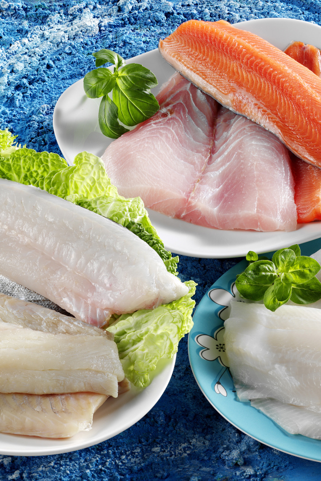 Филе рыбы на тарелках с помидорами и листьями салата