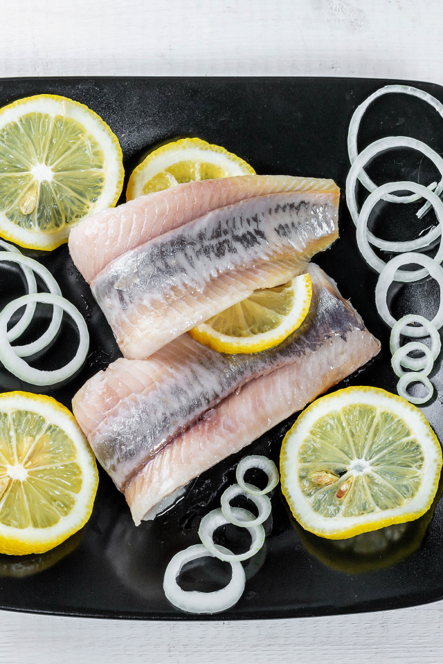 Филе сельди на черной тарелке с луком и лимоном