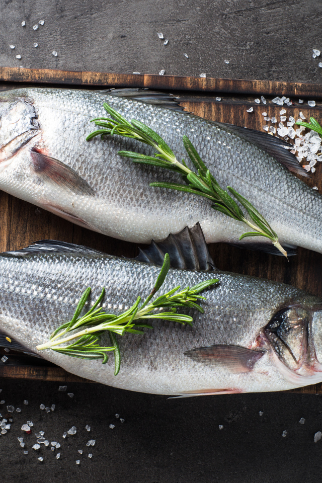 Две свежие рыбины на разделочной доске с солью и веточками розмарина