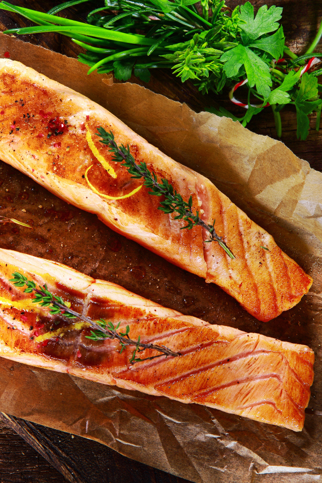 Два куска запеченной рыбы на столе с оливковым маслом и зеленью