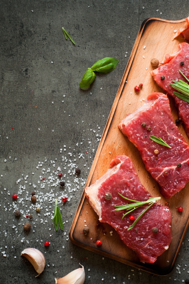 Куски мяса на разделочной доске с зеленью и специями