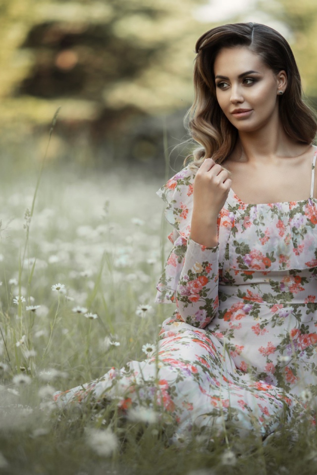 Красивая девушка в сарафане сидит на поляне с ромашками 