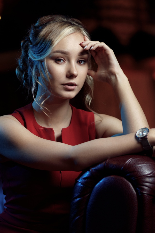 Красивая девушка с часами на руке сидит в кресле