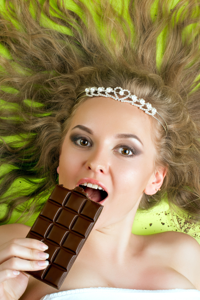 Красивая девушка с украшением в волосах лежит с шоколадкой 
