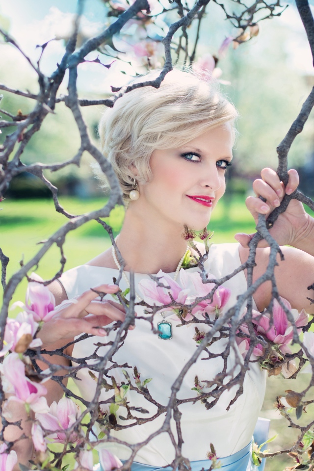 Красивая женщина с короткой стрижкой стоит у цветущей магнолии 