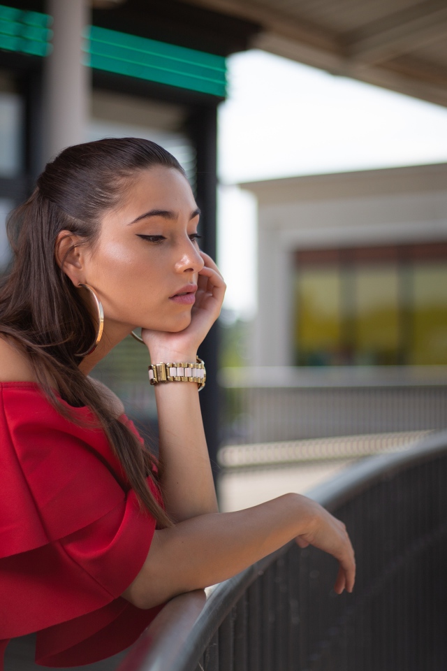 Задуманная девушка в красном платье стоит у перил 