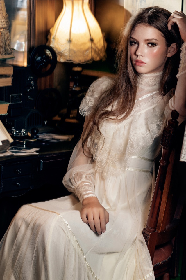 Девушка в красивом белом платье сидит на стуле у стола