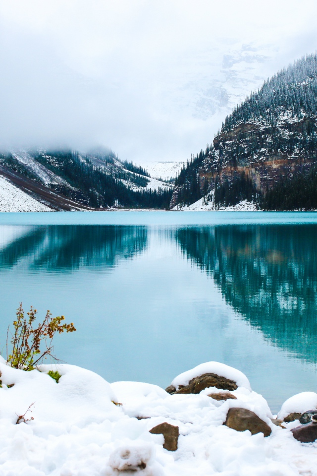 Девушка стоит у голубого озера на заснеженном берегу 