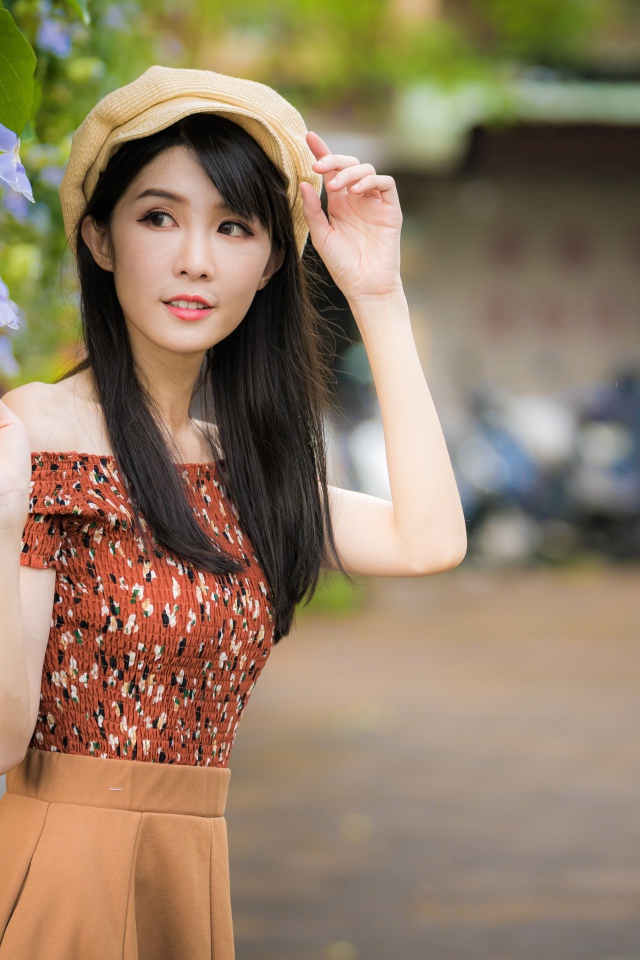 Молодая девушка азиатка в кепке стоит у голубых цветов