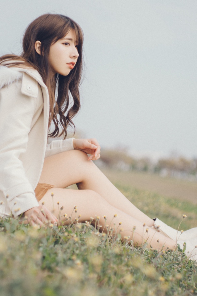 Девушка азиатка в пальто сидит на траве