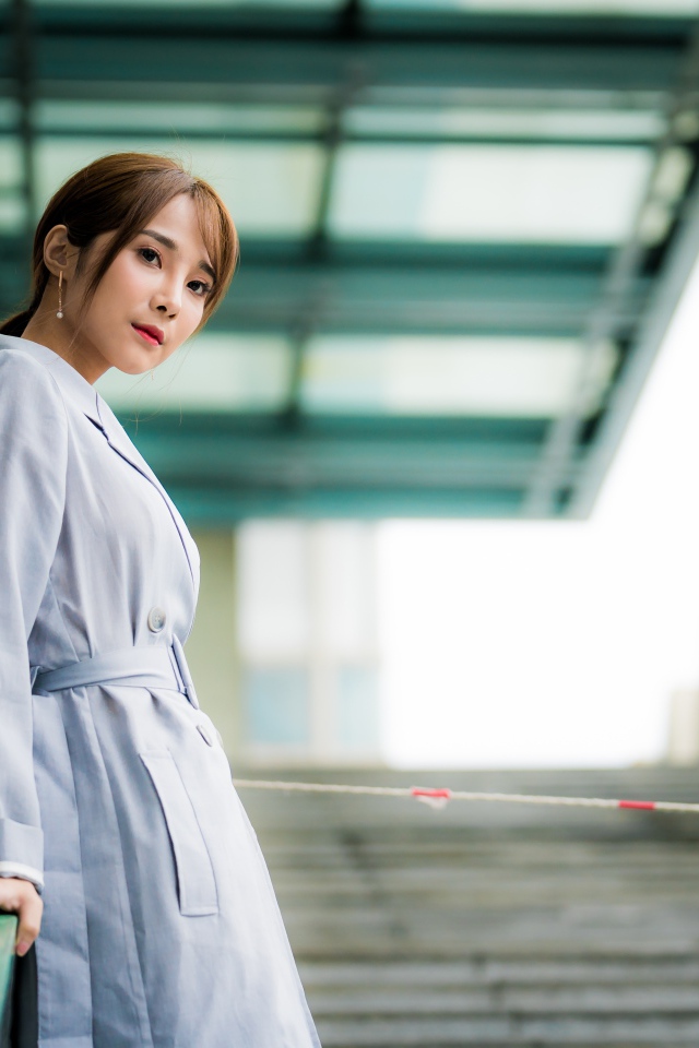 Девушка азиатка в пальто стоит у перил 