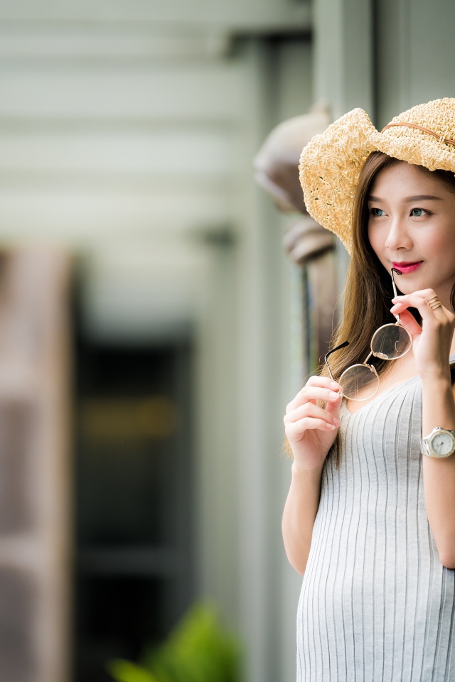 Девушка азиатка в шляпке с очками в руках 