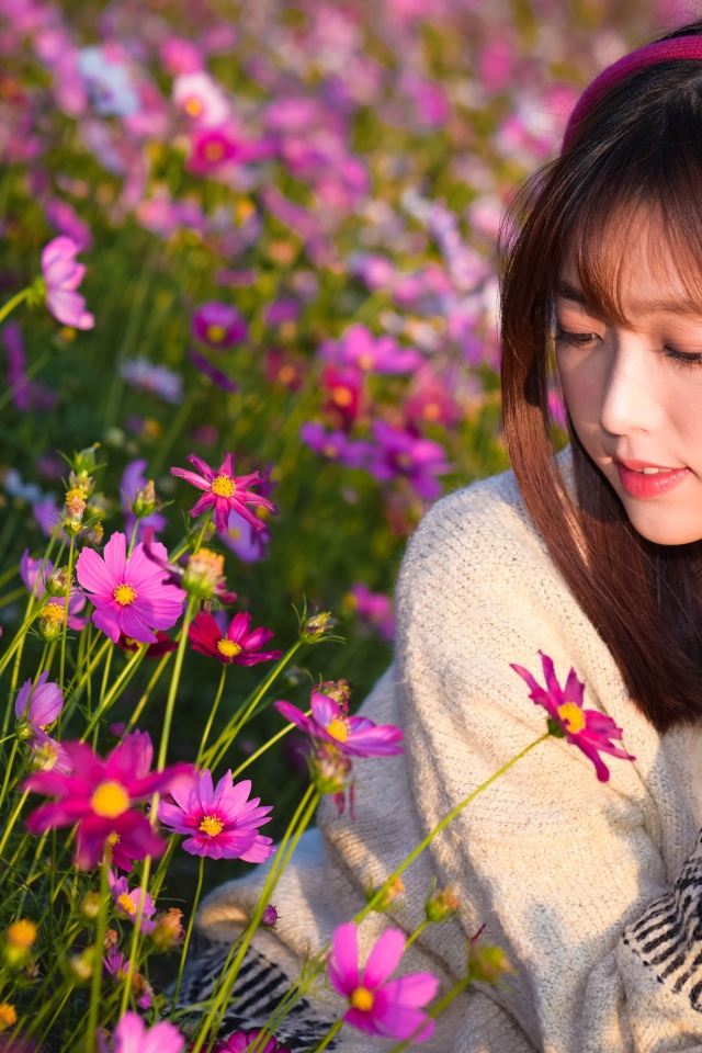 Девушка азиатка в наушниках сидит в цветах космеи