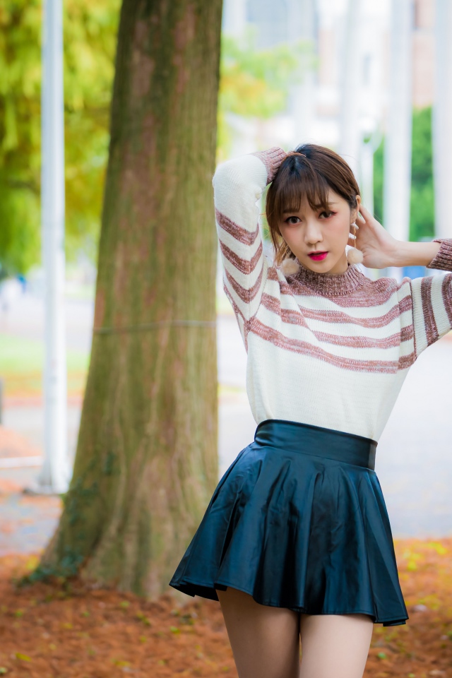 Девушка азиатка стоит в короткой юбке у дерева