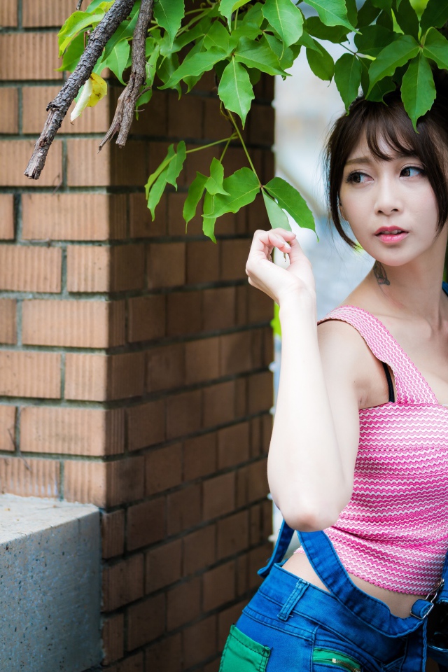 Молодая девушка азиатка у стены с зелеными листьями