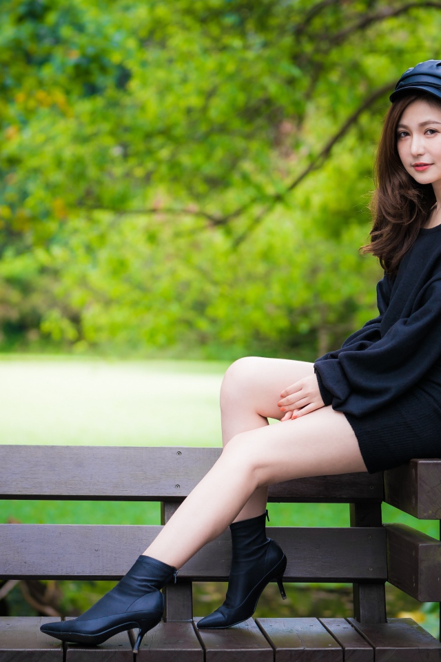 Красивая девушка азиатка в черном платье сидит на деревянной лавке