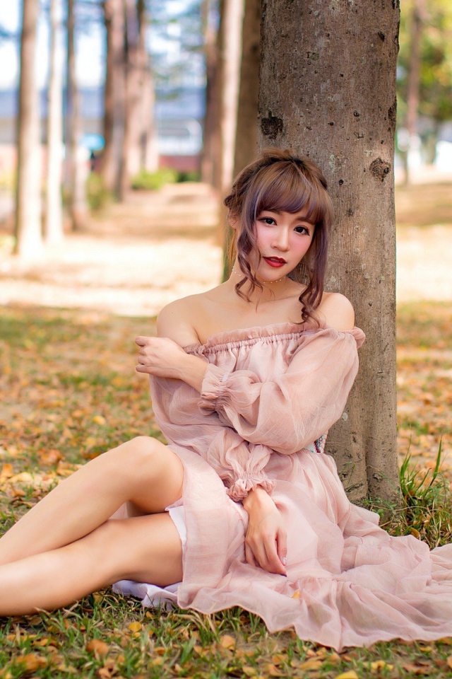 Красивая девушка азиатка в платье сидит под деревом